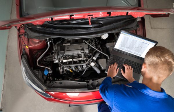 High Angle View Of Mechanic Examining Car Engine With Help Of Laptop